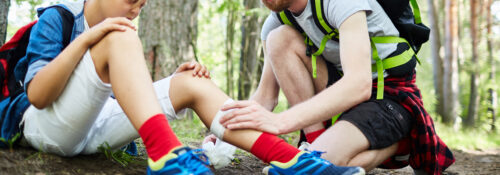 Young scout helping his friend with bandage to bind up injury on leg on their way to camp