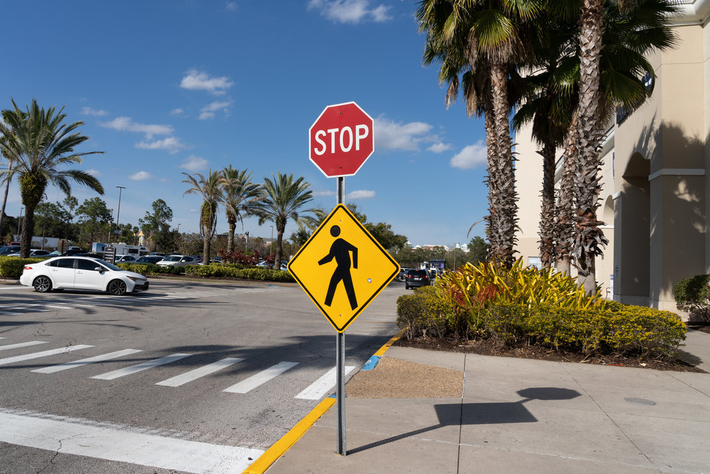 A stop sign with a Pedestrian Crossing Sign outside a shopping mall is shown in Orlando, Florida, USA.
